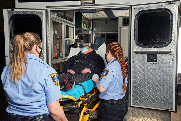 Two female first responders loading a stretcher with a person into the back of an ambulance
