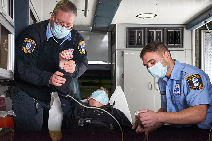 Two male first responders checking a person's vitals in the back of an ambulance