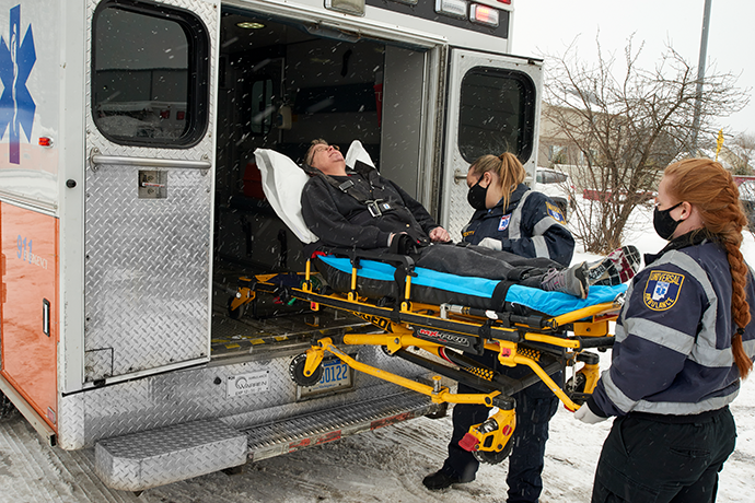 Two female first responders loading a stretcher with a person into the back of an ambulance while it snows