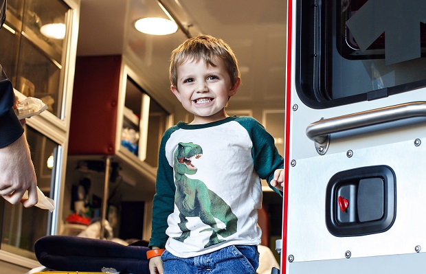 Smiling little boy wearing t-rex shirt standing in the back of an ambulance