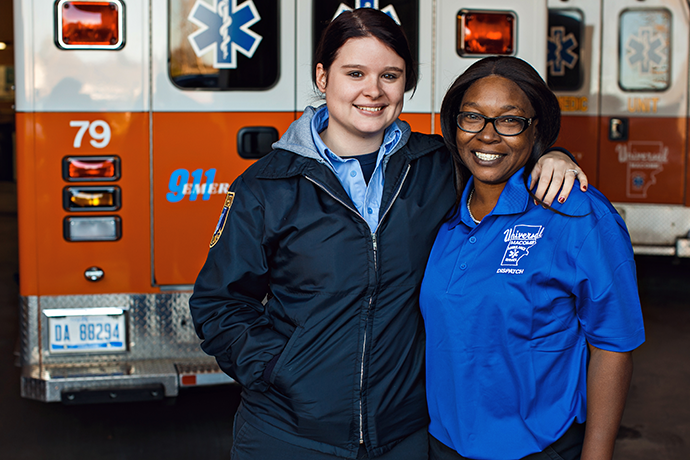 An emergency responder and a Universal Ambulance Service employee posing together and smiling at the camera in front of an ambulance